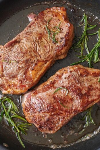 Closeup of pan-seared steaks in a skillet with sprigs of rosemary.