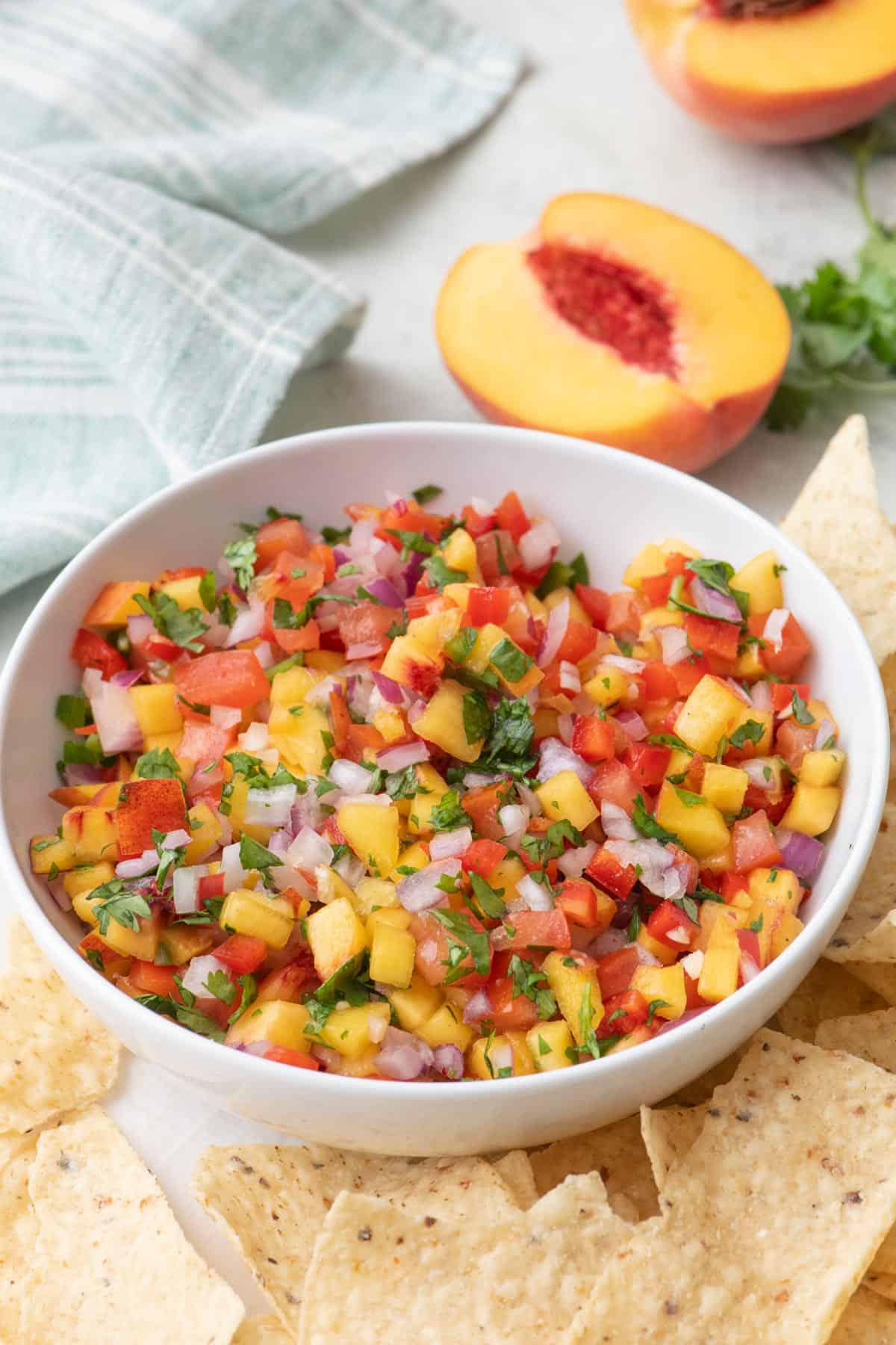 Bowl of peach salsa with tortilla chips, peaches, and fresh cilantro nearby.