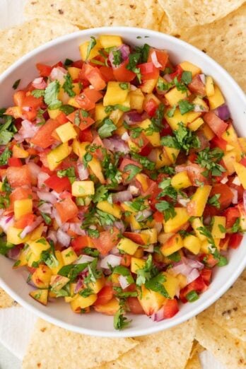 Bowl of peach salsa on a plate of tortilla chips.