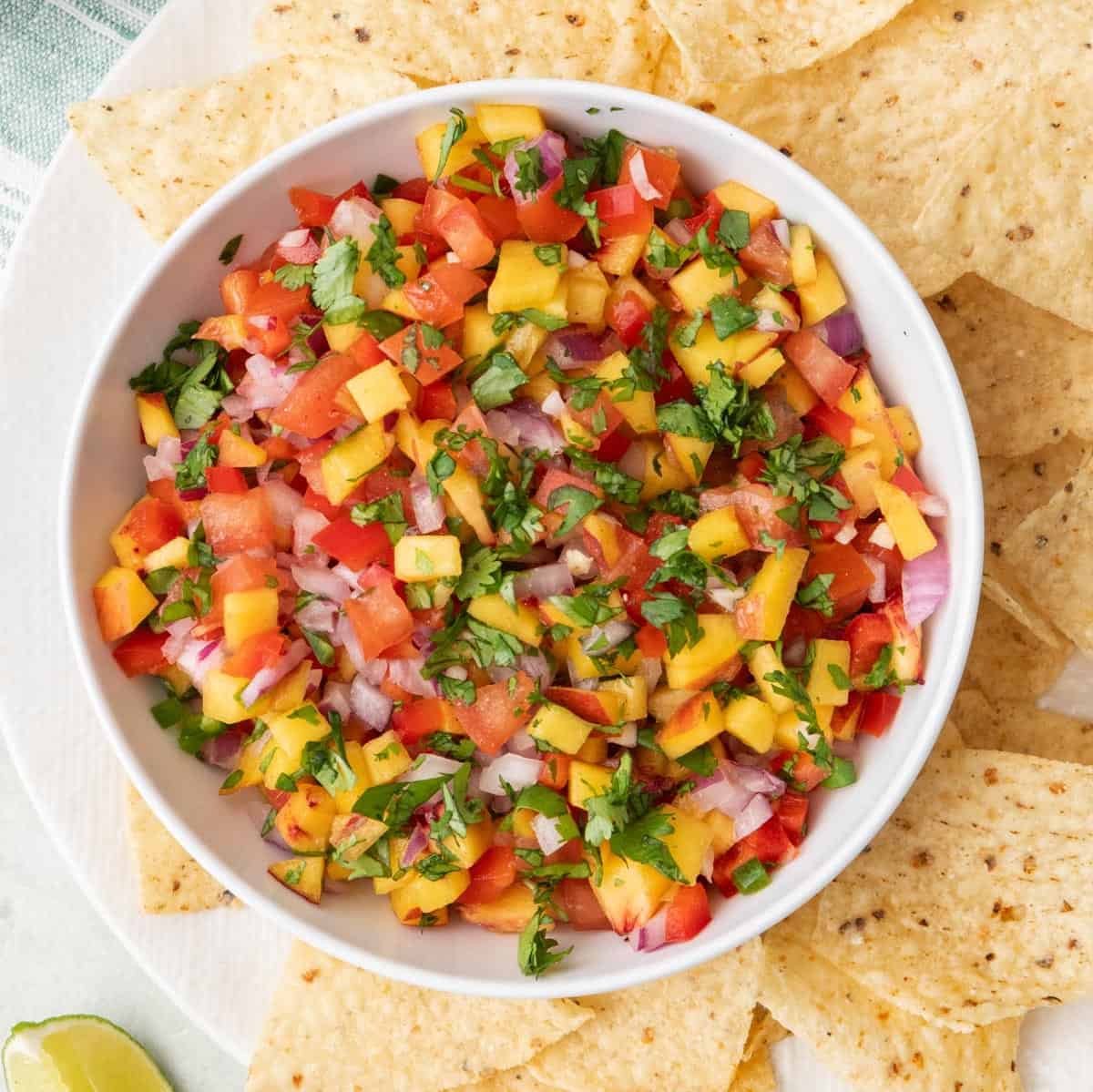 Bowl of peach salsa on a plate of tortilla chips.
