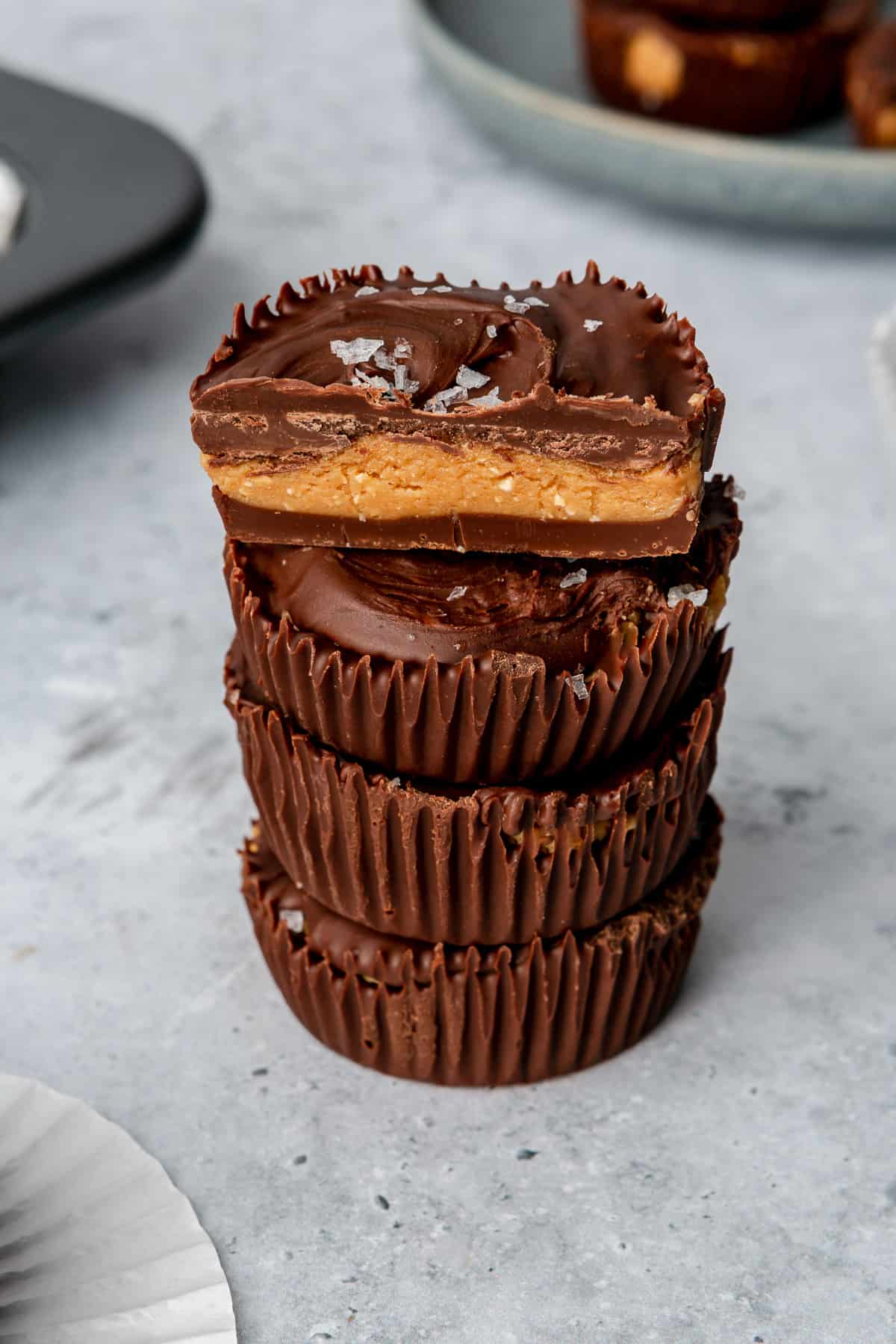 Peanut butter cups with flaky salt stacked on a marble counter, the top one cut in half.