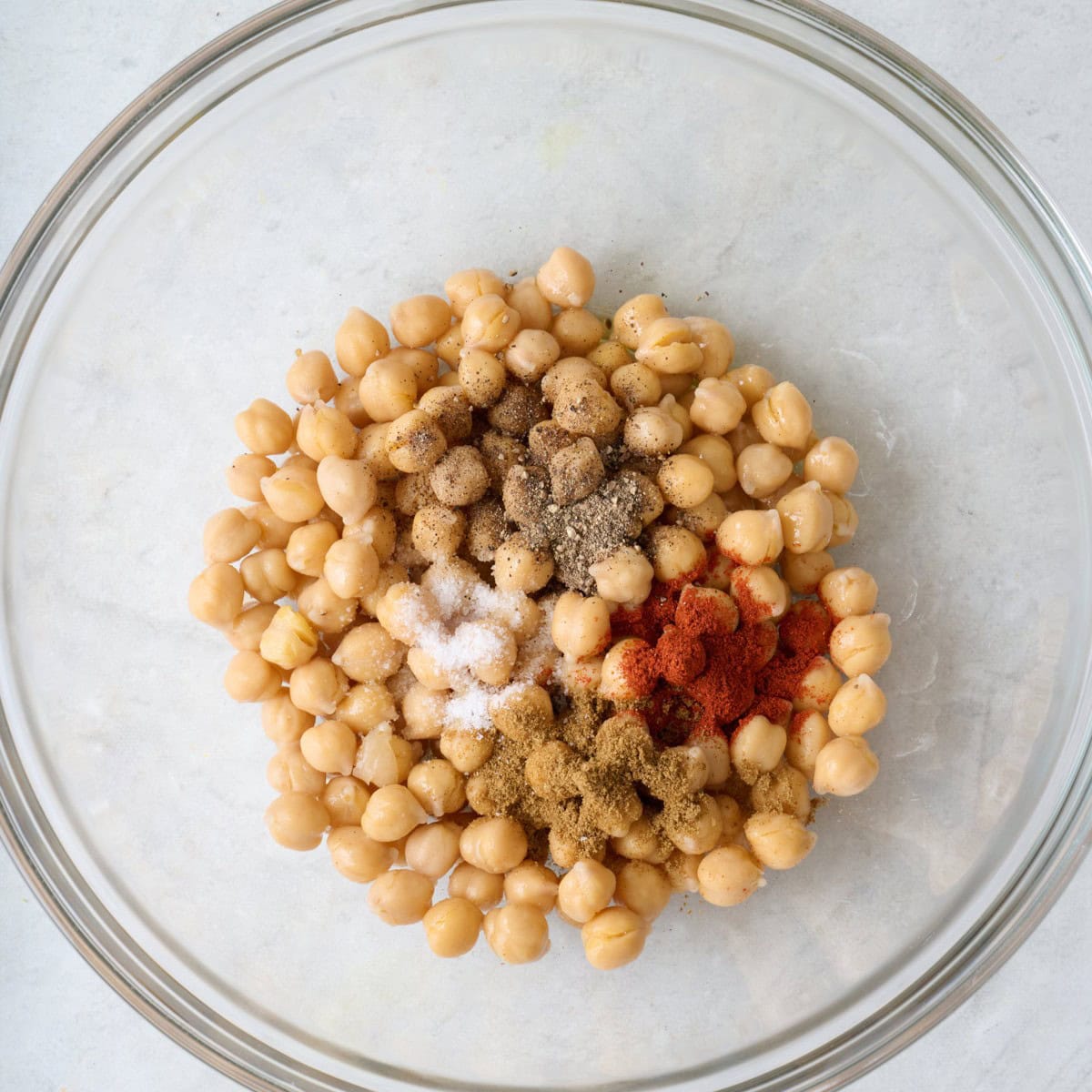 Chickpeas in bowl with oil, cumin, paprika, salt and pepper added.