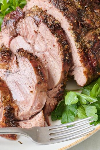 Sliced roasted leg of lamb on a plate with fresh parsley garnish and a fork.