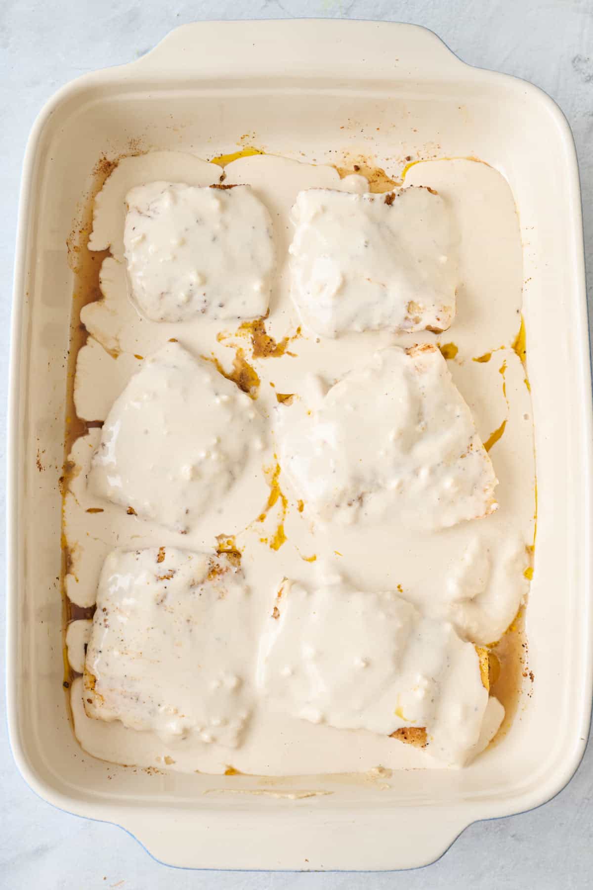 Fish in baking dish with tahini sauce poured over it.