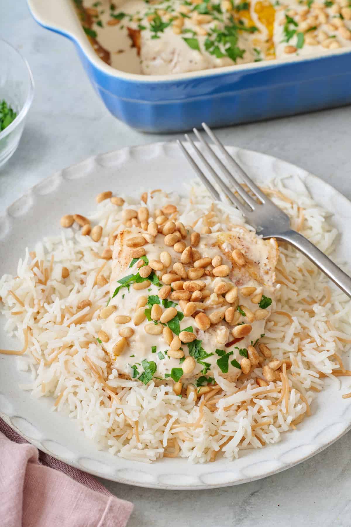 A serving of samke harra on a small plate over Lebanese rice with pine nuts and parsley on top.