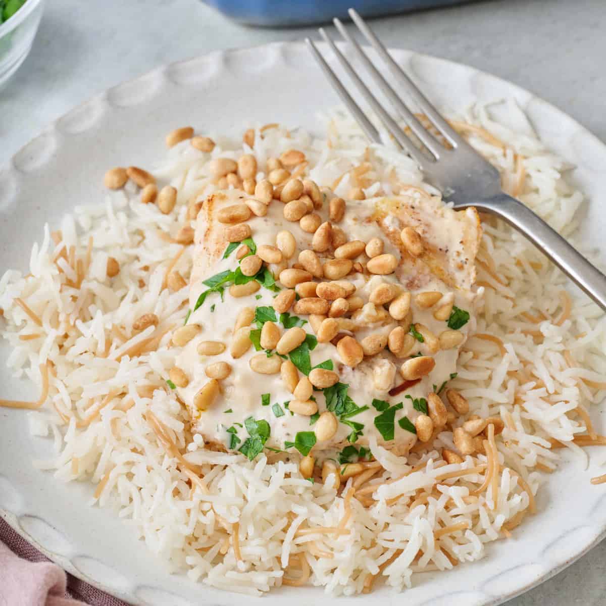 Closeup of samke harra on a small plate over Lebanese rice with pine nuts and parsley on top.