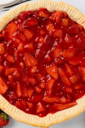 Beautiful strawberry pie in a pie tin with fresh strawberries nearby.