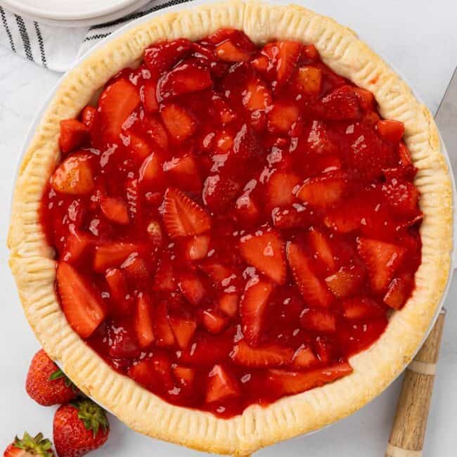 Beautiful strawberry pie in a pie tin with fresh strawberries nearby.