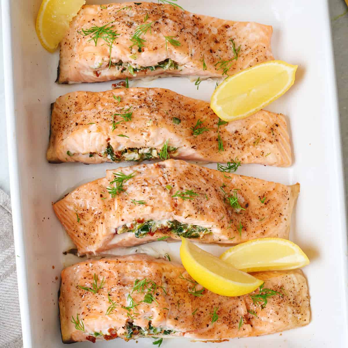 Stuffed baked salmon in a white baking dish garnished with lemon slices.