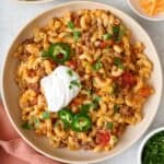 Closeup of bowl of taco pasta topped with jalapeños, fresh cilantro, and a dollop of sour cream.