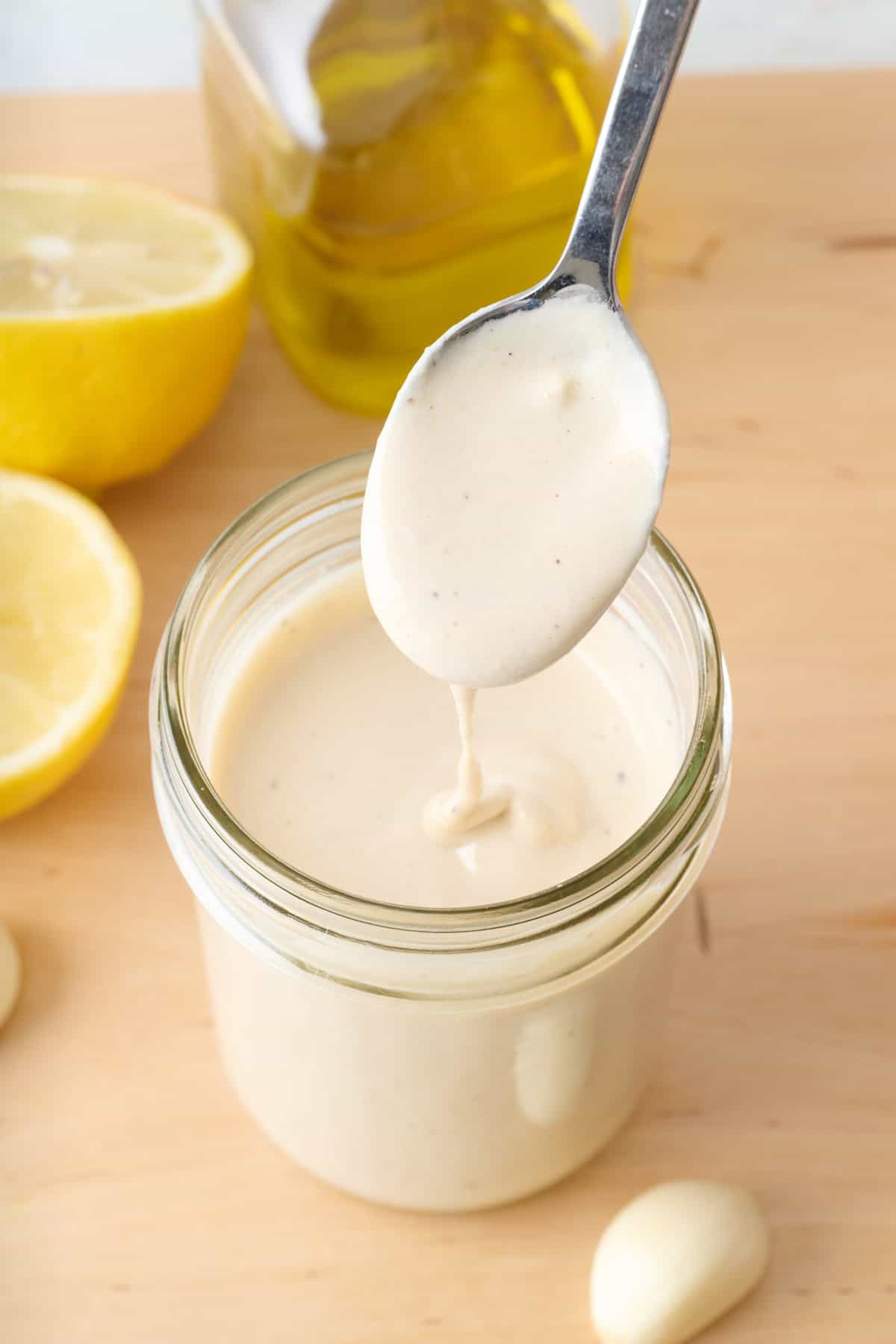 Spoon lifting up tahini dressing from a small glass jar with dressing drizzling back into it.