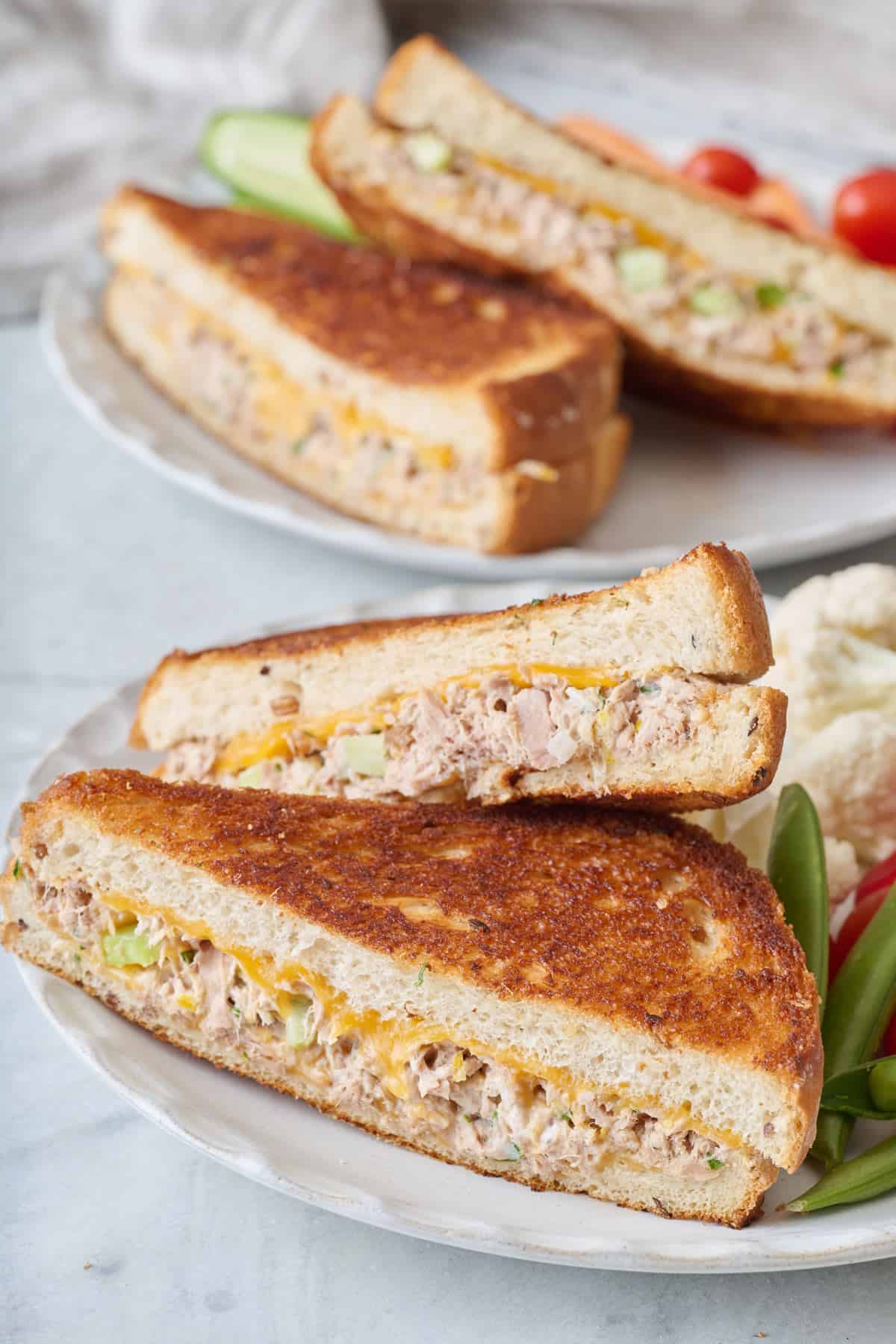 Two tuna melt sandwiches served on a plate with fresh vegetables.