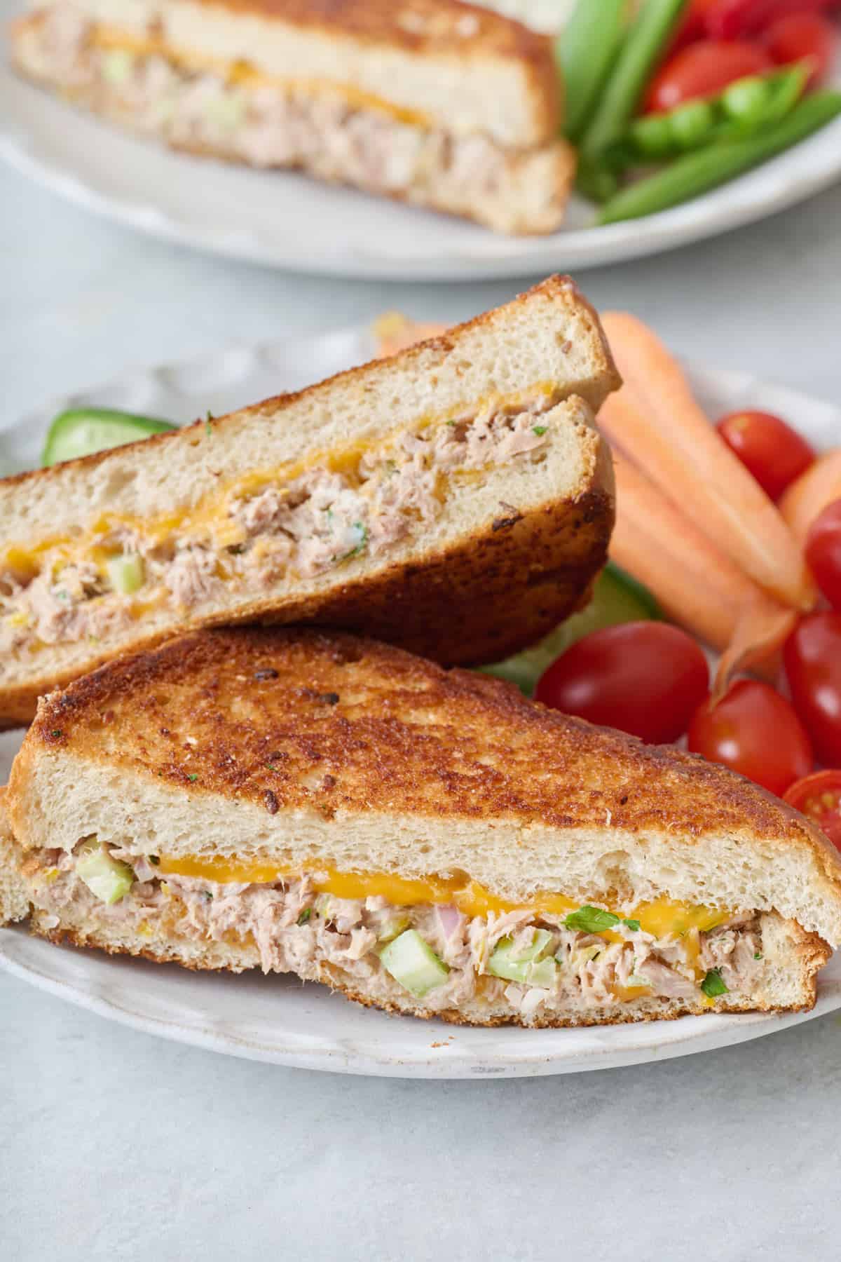 Close up of a tuna melt sandwich cut in half on a plate with veggies.