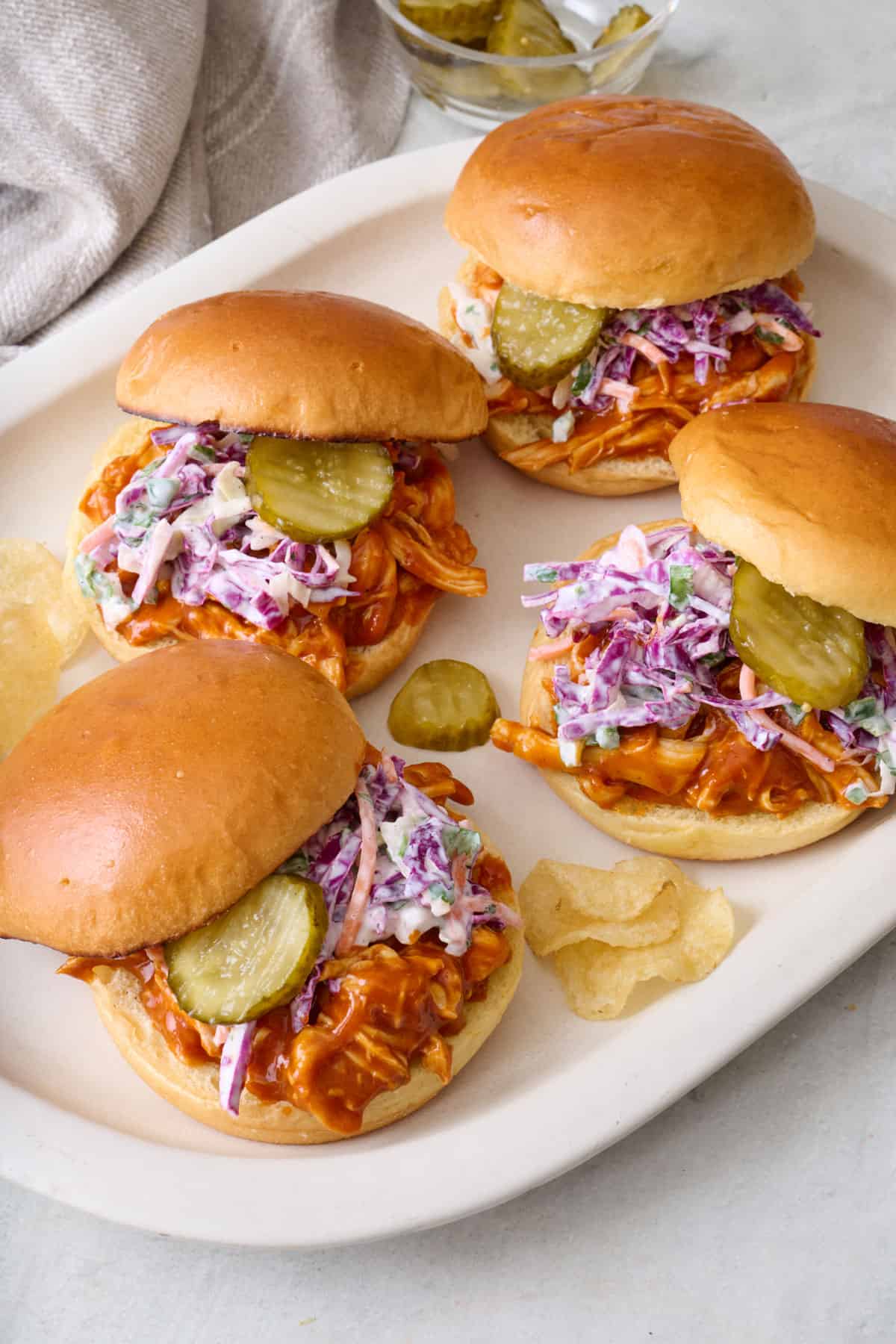 Four bbq chicken sandwiches on a platter, topped with a homemade coleslaw.
