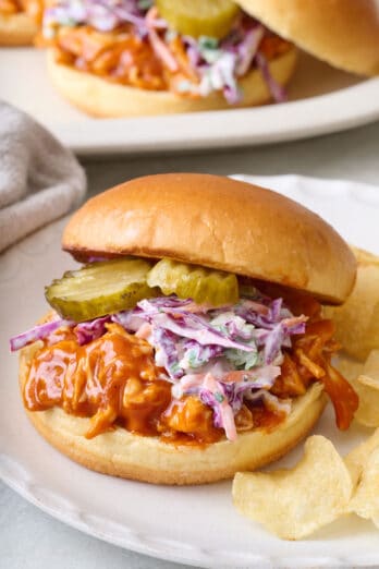 Shredded bbq chicken sandwich on a brioche bun with a homemade coleslaw and sliced pickles.