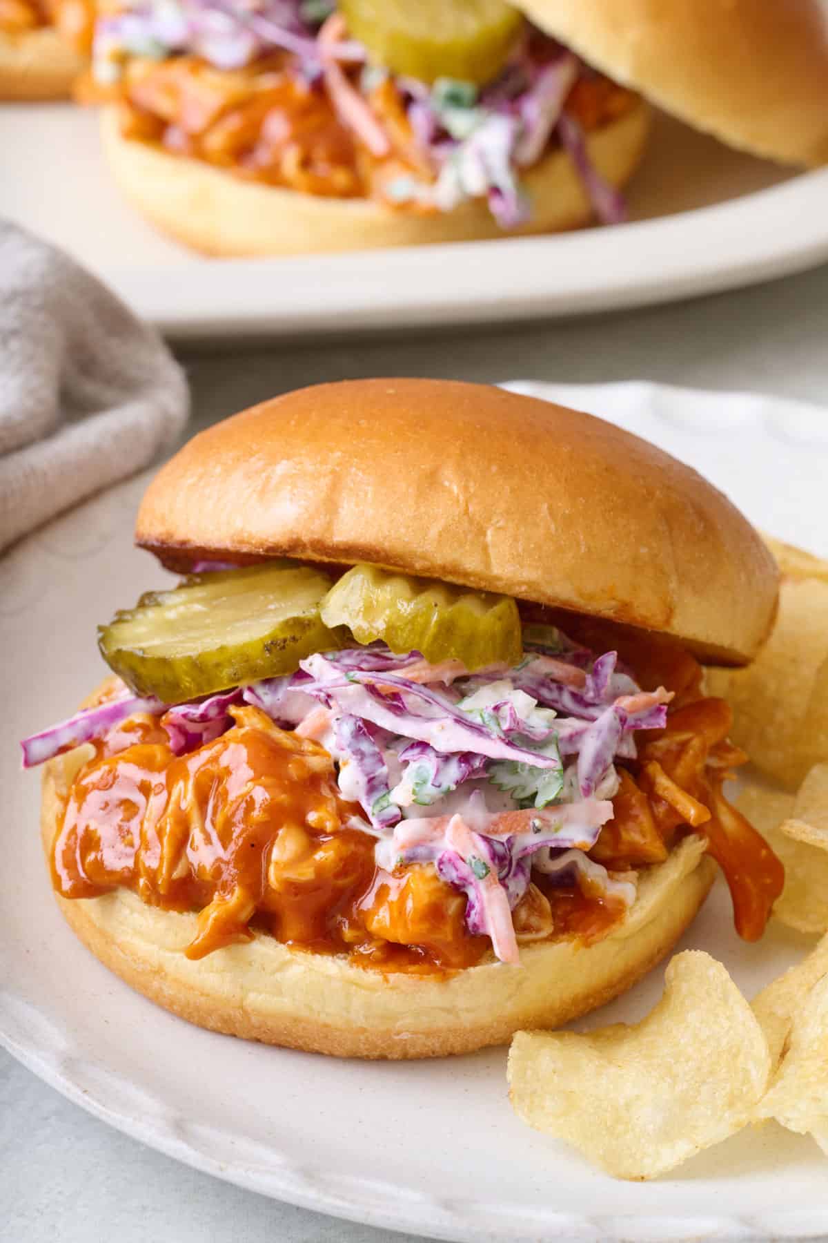 Shredded bbq chicken sandwich on a brioche bun with a homemade coleslaw and sliced pickles.