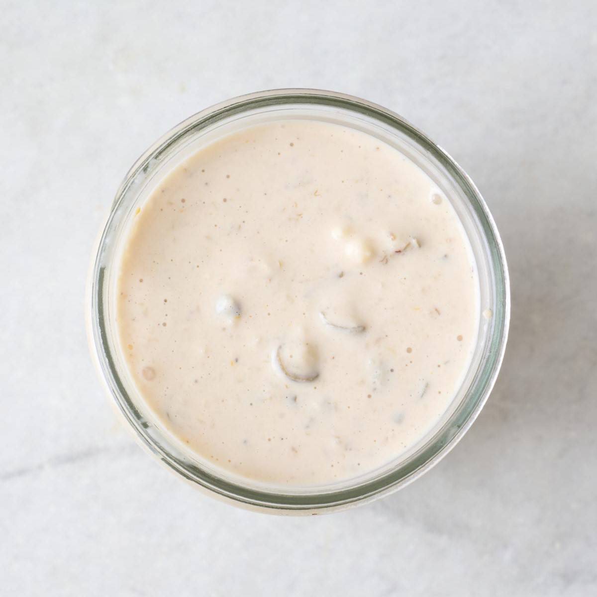 Creamy Caesar salad dressing with capers in a glass jar.