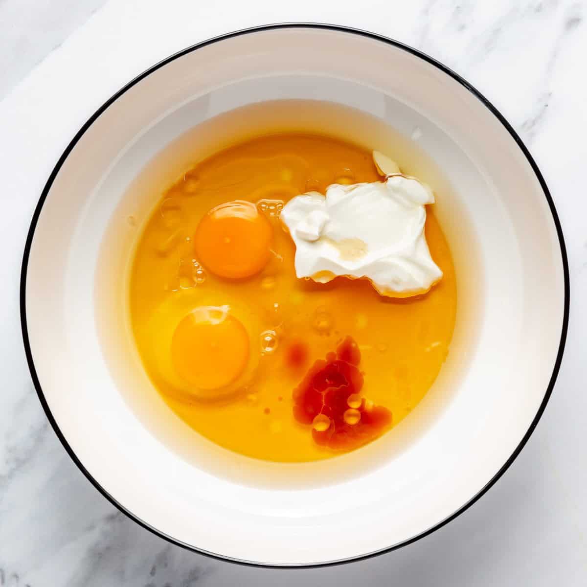 Oil, eggs, maple syrup, and Greek yogurt in a bowl before mixing.