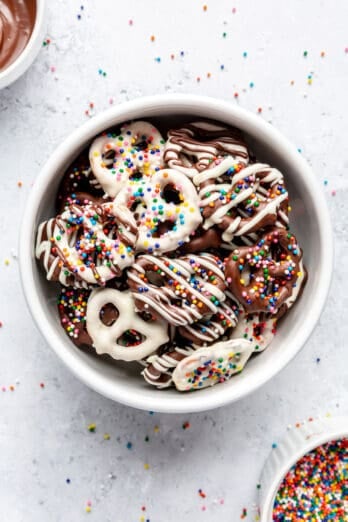 Overhead shot of bowl of chocolate-covered pretzels with rainbow sprinkles and chocolate drizzles.