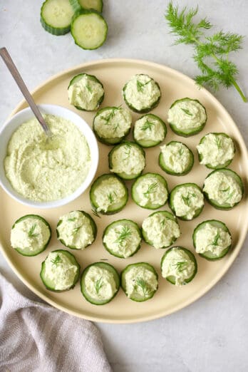 Tray of cucumber canapes and whipped feta dip in small bowl; fresh cucumber slices and dill nearby.