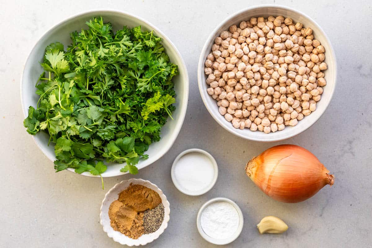 Ingredients for recipe: fresh cilantro and parsley, dry chickpeas, spices, baking powder, garlic clove, onion.