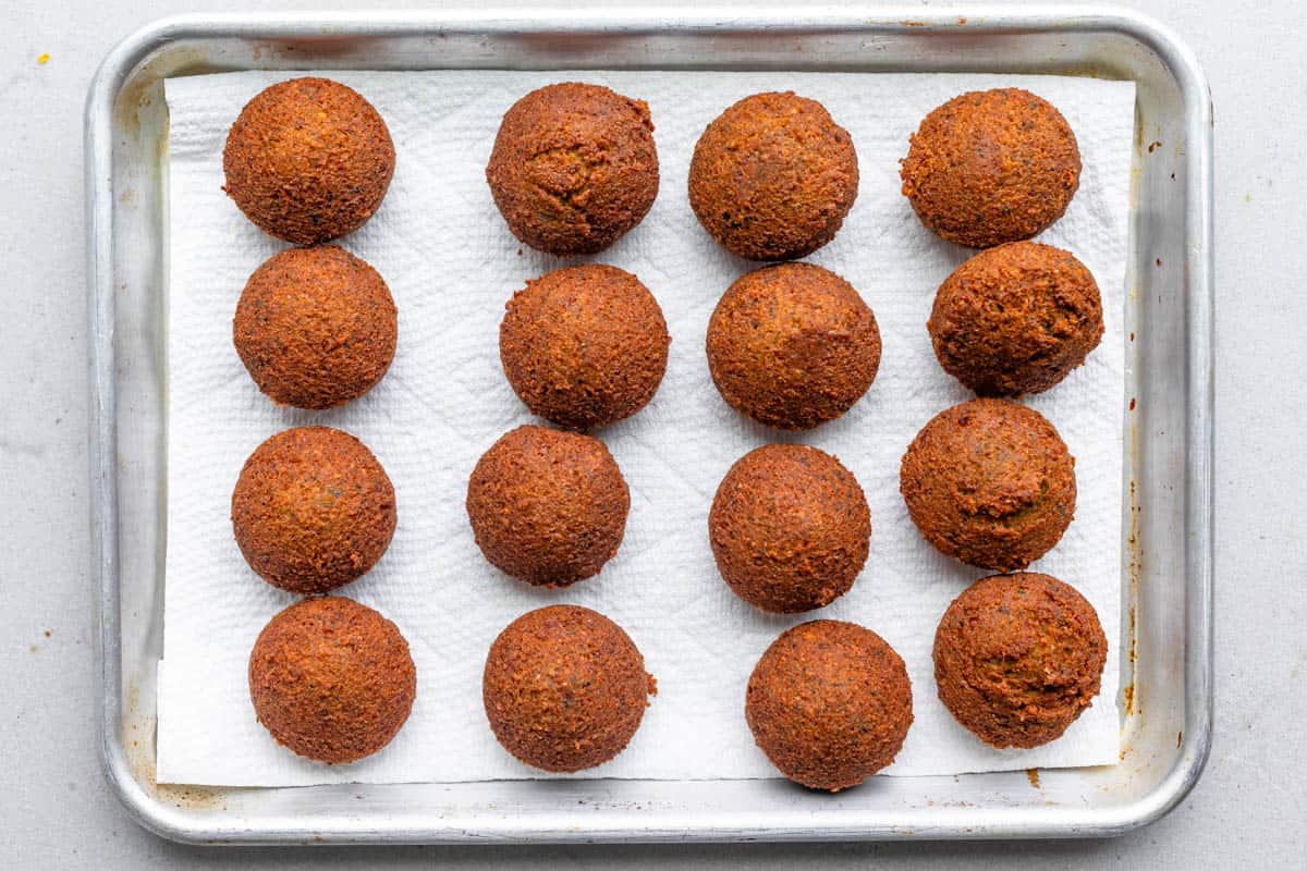 Fried falafel on a paper towel lined sheet pan after frying.