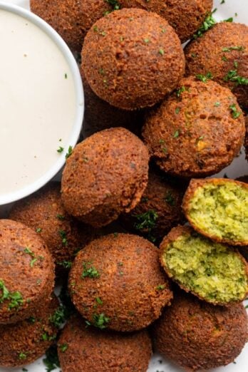 Homemade fried falafel on a plate with a small dish of tahini sauce.