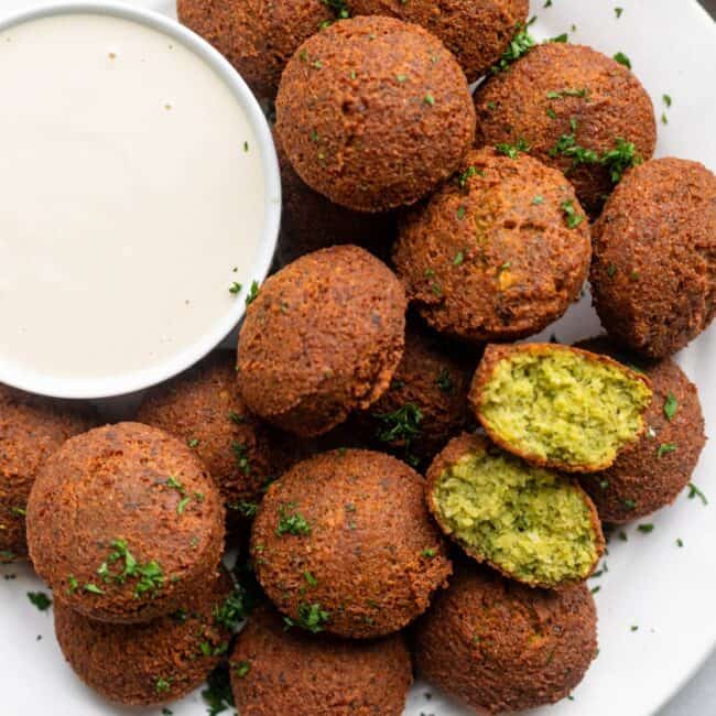Homemade fried falafel on a plate with a small dish of tahini sauce.
