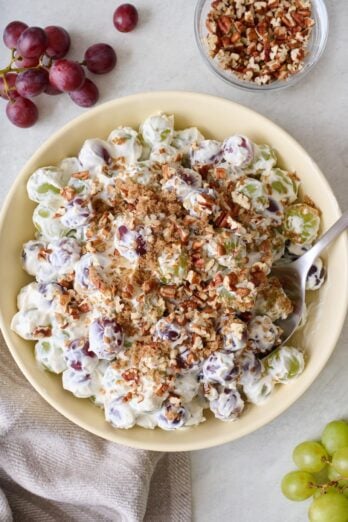 Grape salad topped with pecans in a bowl with fresh grapes, chopped pecans, and linen napkin nearby.