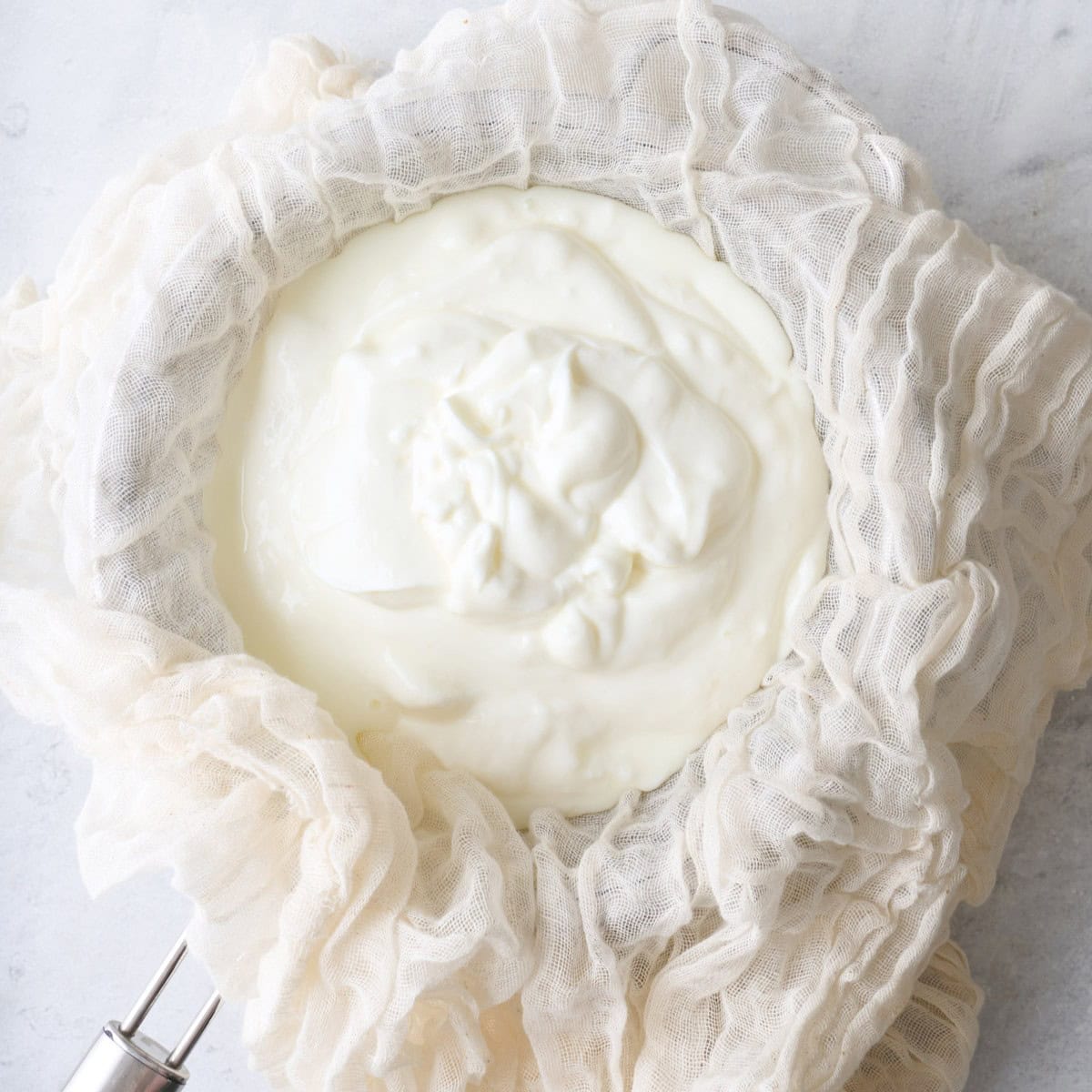 Cheesecloth over a fine mesh strainer set on top of a bowl with the yogurt and salt.