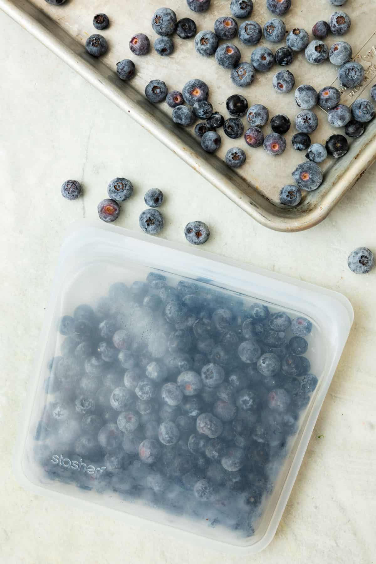 How to freeze blueberries: Stasher reusable silicone bag filled with frozen blueberries with rimmed tray of frozen blueberries nearby.