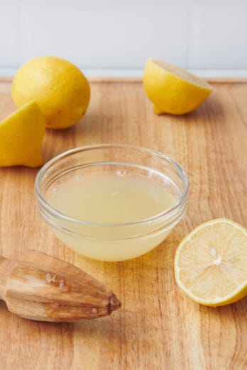 A small bowl of lemon juice with fresh lemons and a citrus reamer nearby.