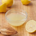 Lemon juice in a small bowl with citrus reamer and fresh lemons nearby.