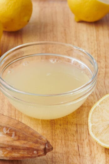 Lemon juice in a small bowl with citrus reamer and fresh lemons nearby.