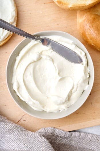 Small bowl of whipped cream cheese with spreading knife after following how to make whipped cream cheese tutorial; toasted bagels nearby.