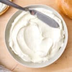 Whipped cream cheese in a small white bowl with a spreading knife.