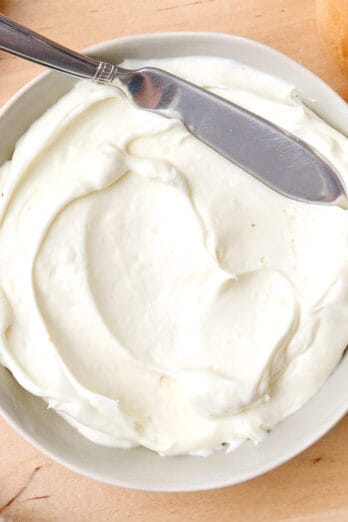 Whipped cream cheese in a small white bowl with a spreading knife.