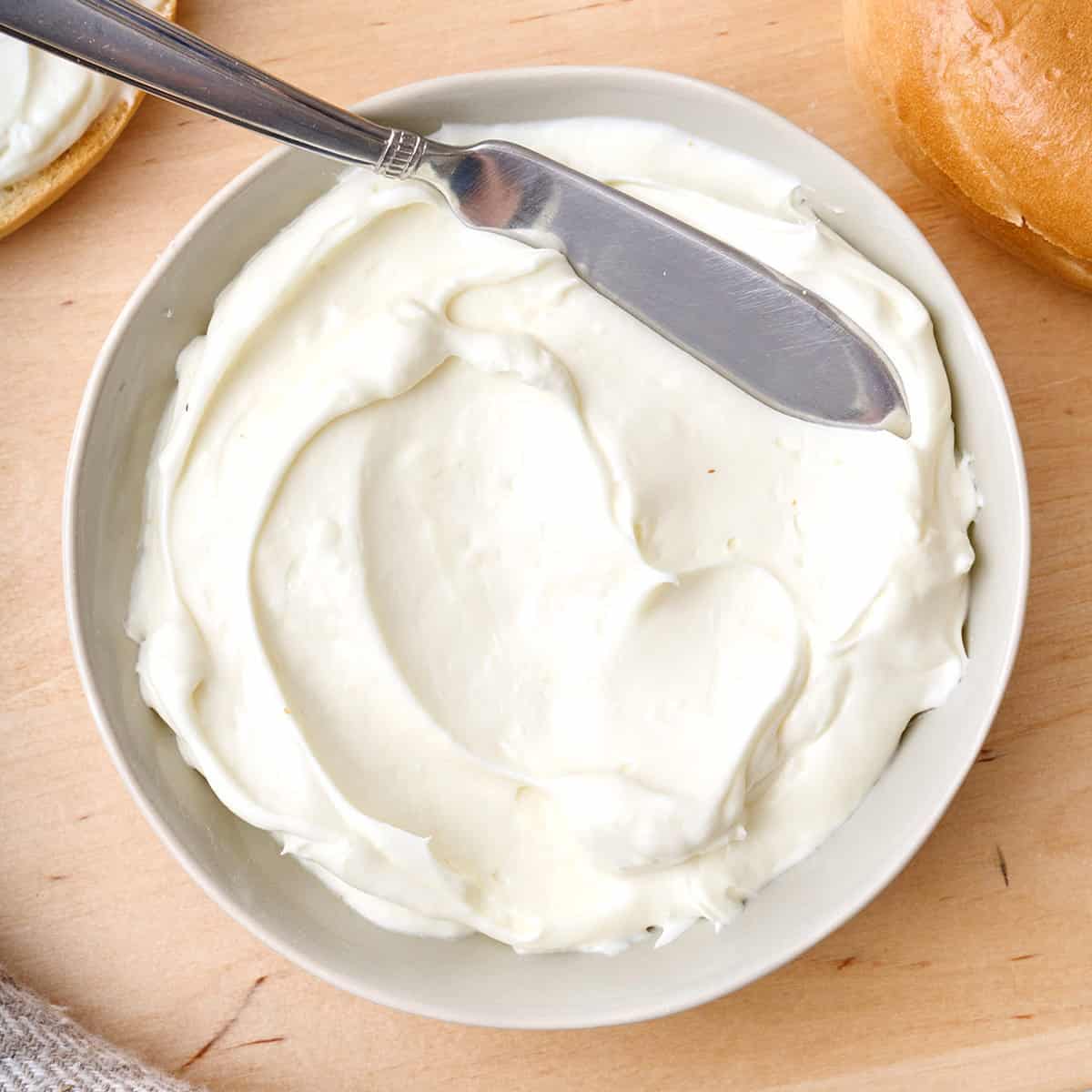 Whipped cream cheese in a small white bowl with a spreading knife.