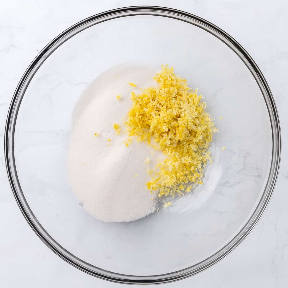 Granulated sugar and lemon zest in a large glass mixing bowl.