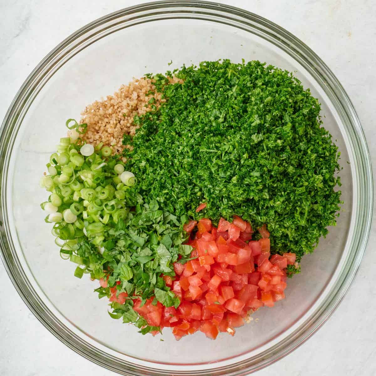 Chopped parsley, mint, green onions, tomatoes and quinoa in a bowl.