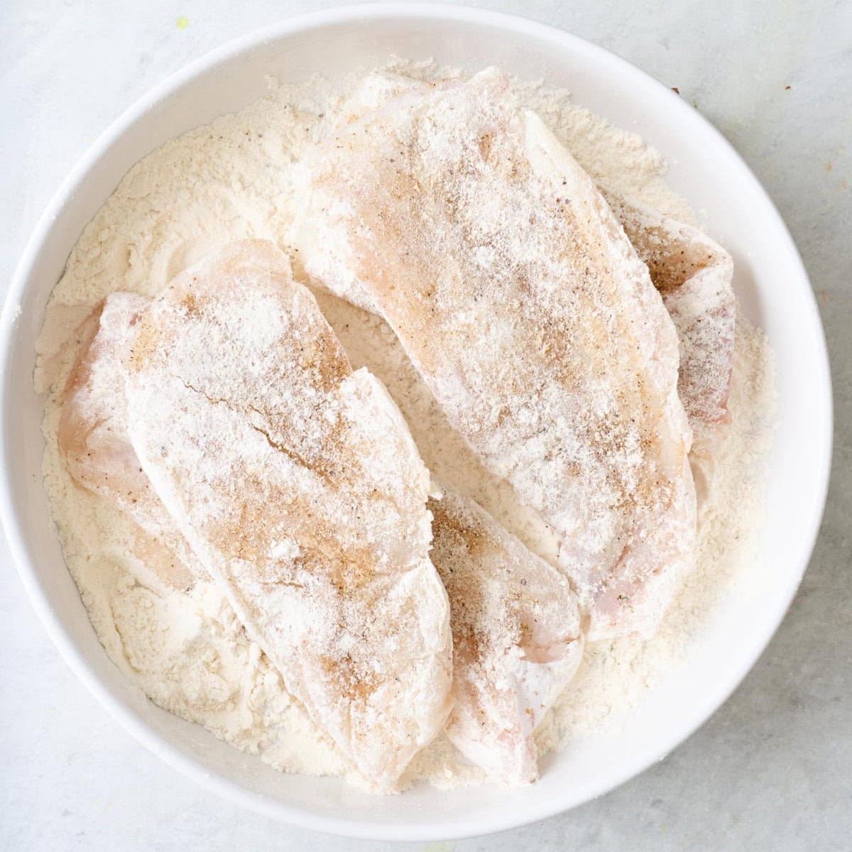 Seasoned fish tossed in a bowl of flour.