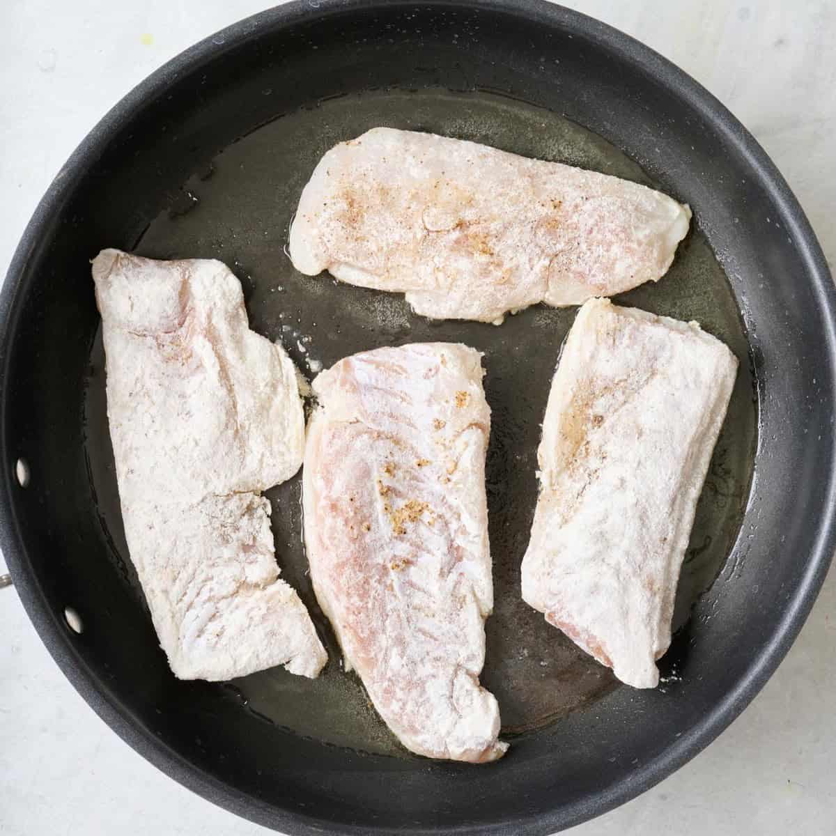 Floured fish in a skillet before flipping.