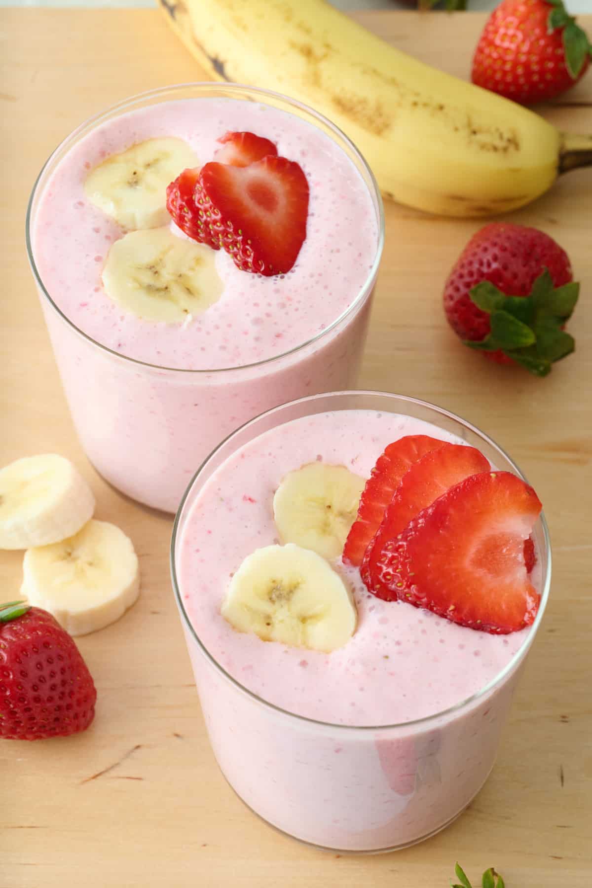Two glasses of strawberry banana smoothie garnished with extra sliced fruit on top.