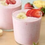 Strawberry banana smoothie divided into two small glasses with extra strawberry and banana slices on top.