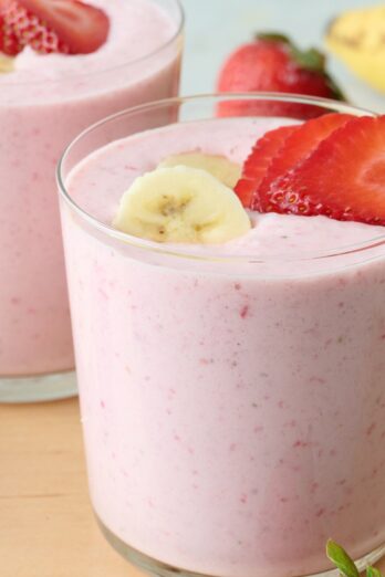 Strawberry banana smoothie divided into two small glasses with extra strawberry and banana slices on top.