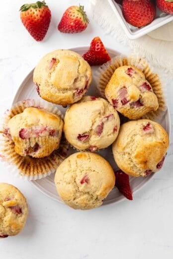Fresh strawberry muffins on a plate with more berries nearby.