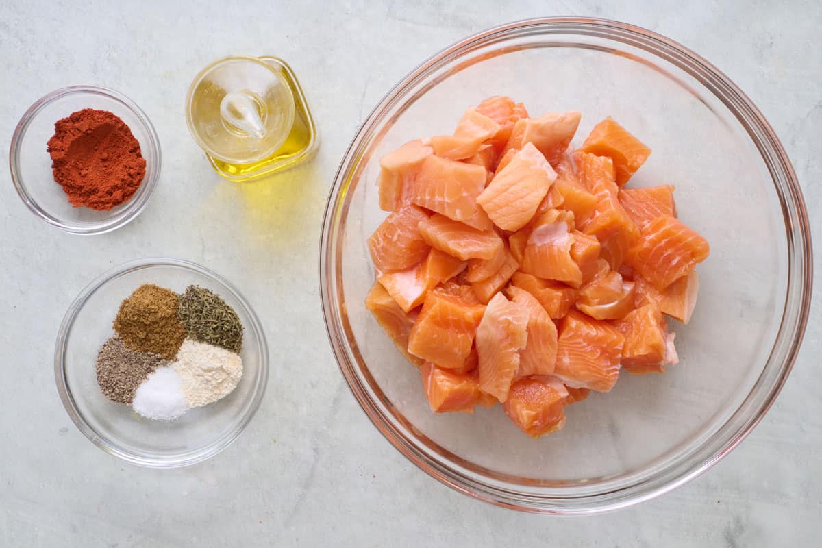 Ingredients for recipe: bowl of salmon cut into cubes, spices, and oil.