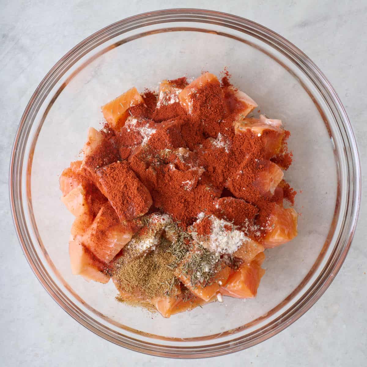 Salmon pieces in a bowl with spices, before tossing together.