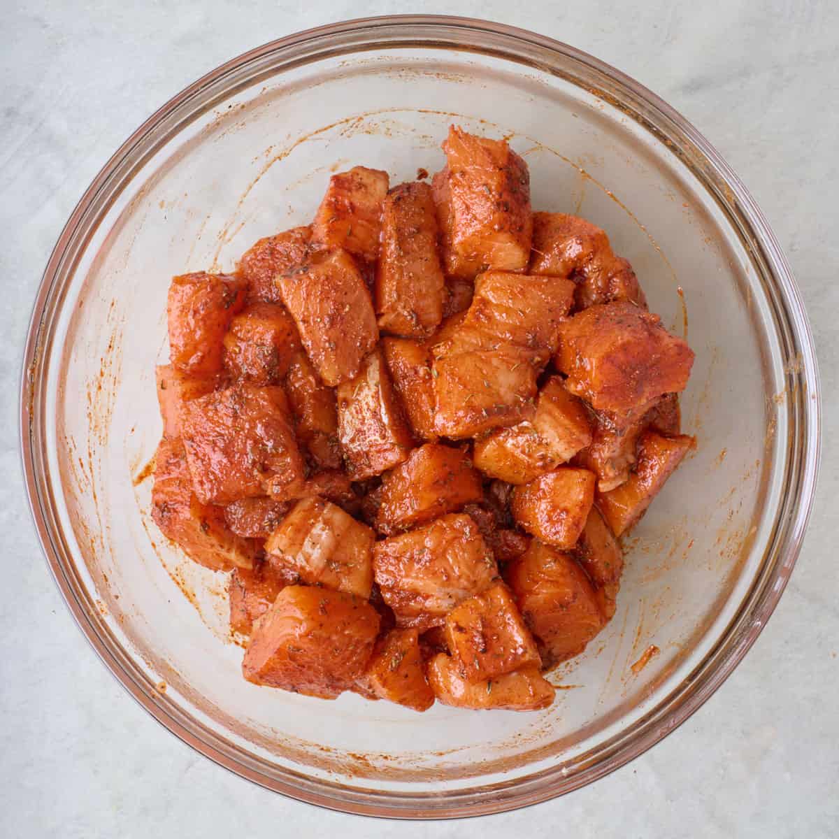 Pieces of fish in a bowl tossed with spices and oil.