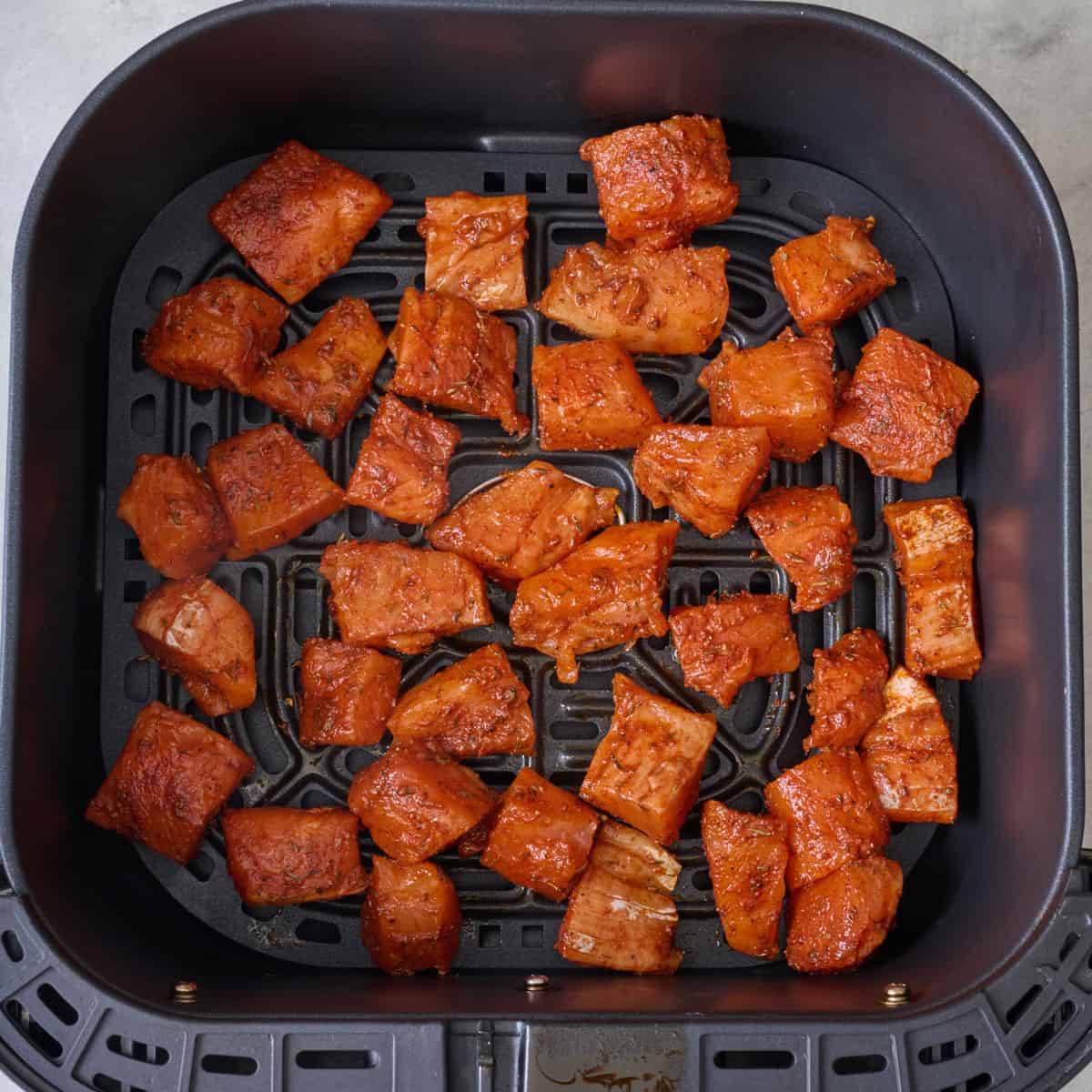 Seasoned pieces of salmon in an air fryer basket before cooking.